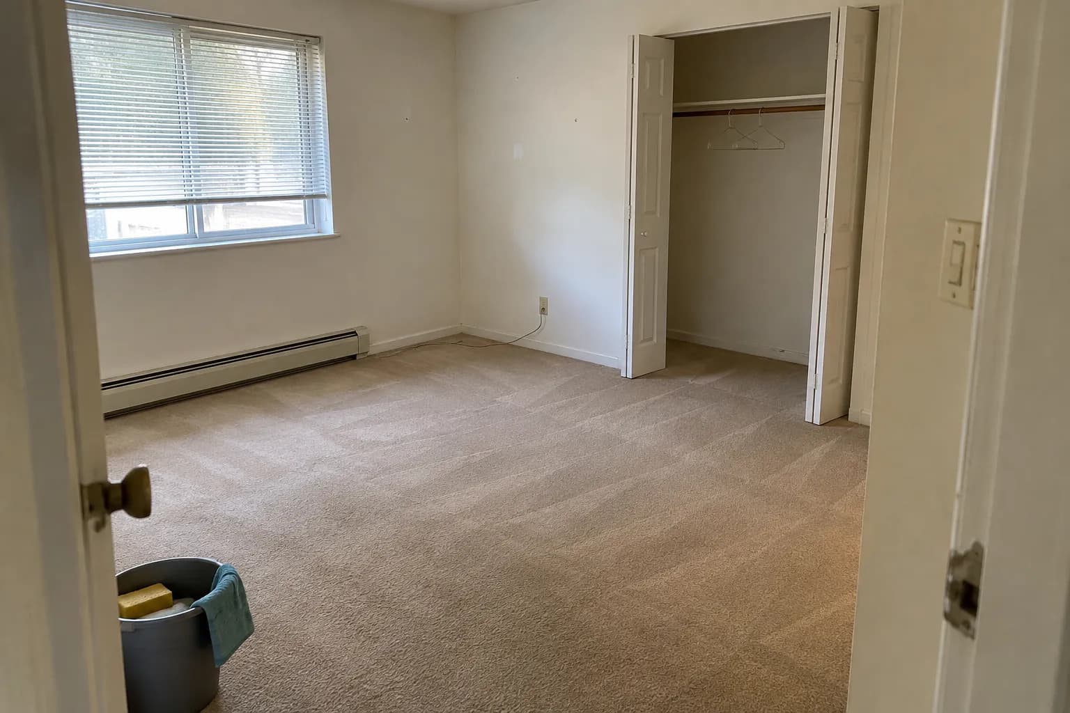 Empty apartment bedroom with fresh vacuum lines in the beige carpet and an open, empty closet