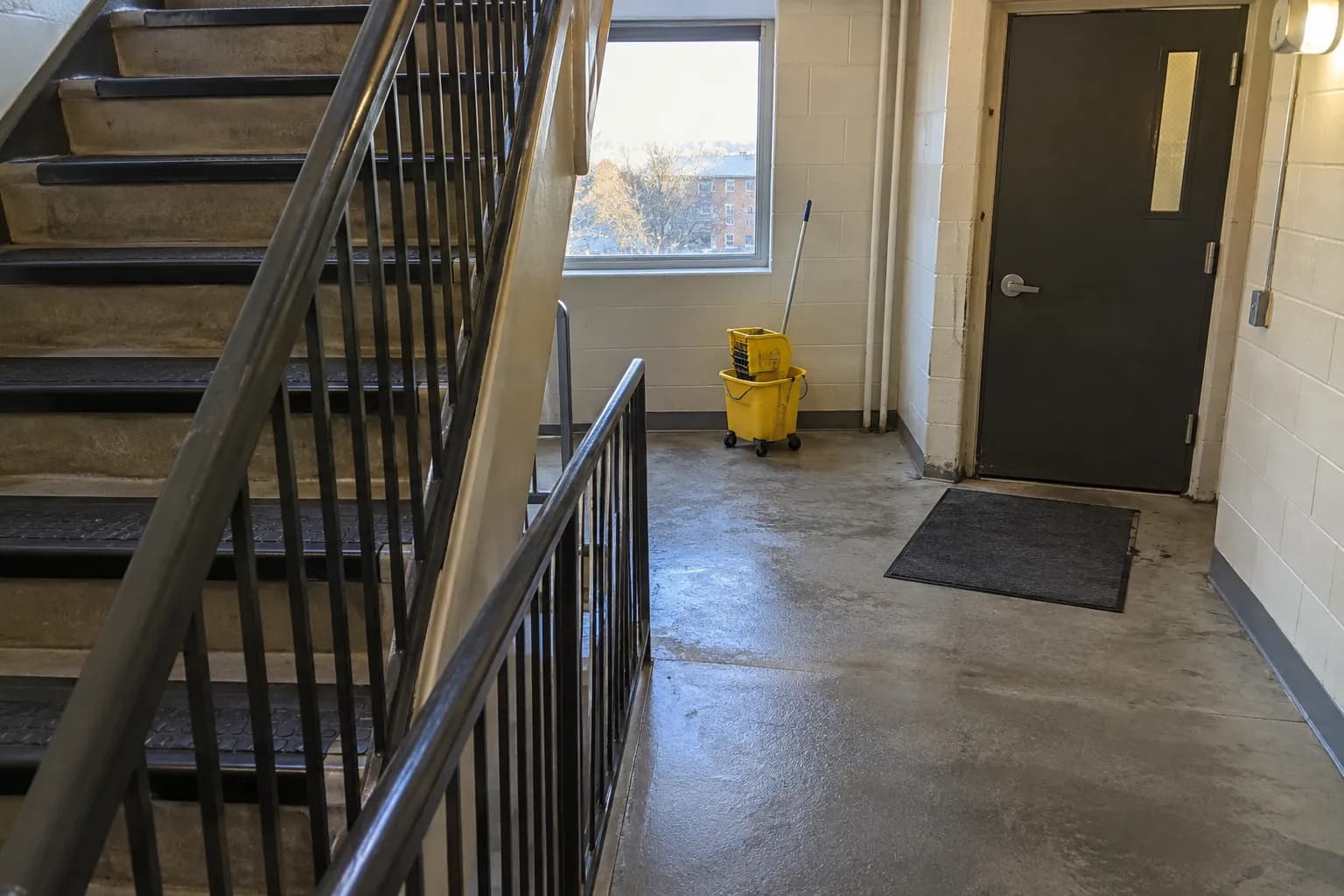 A freshly mopped apartment building stairwell with a mop bucket on the landing