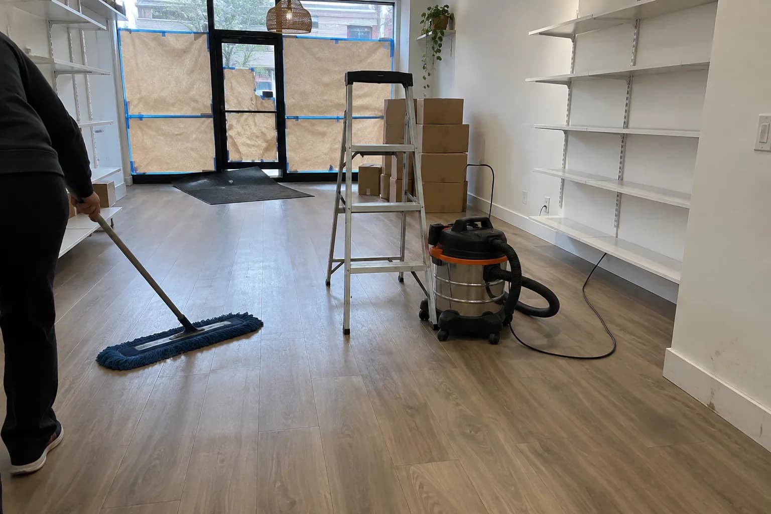 A newly renovated retail space being dust-mopped, with a ladder and shop vacuum