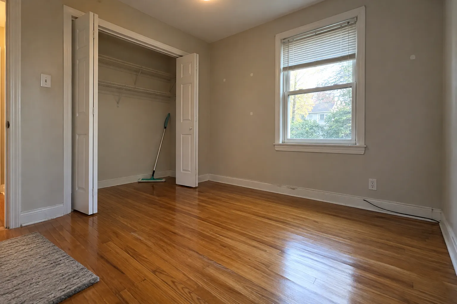 An empty bedroom with freshly mopped hardwood and the closet doors open, ready for move-in