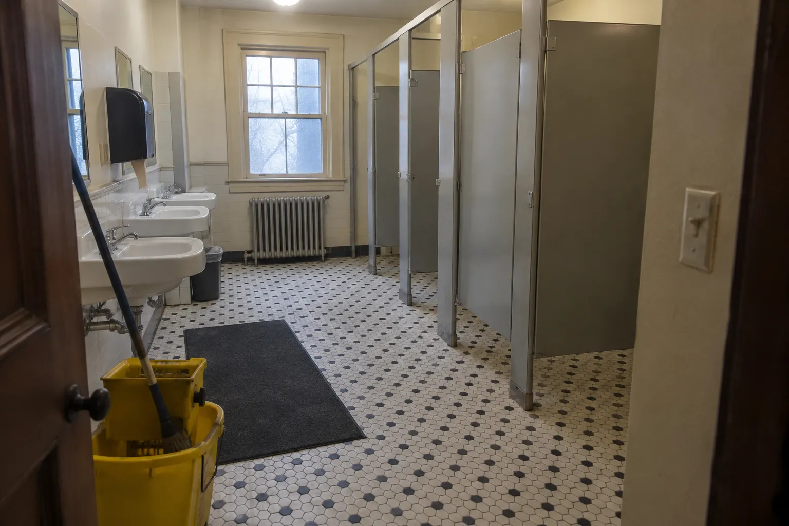 An older church restroom with hexagon floor tile and a mop bucket at the door