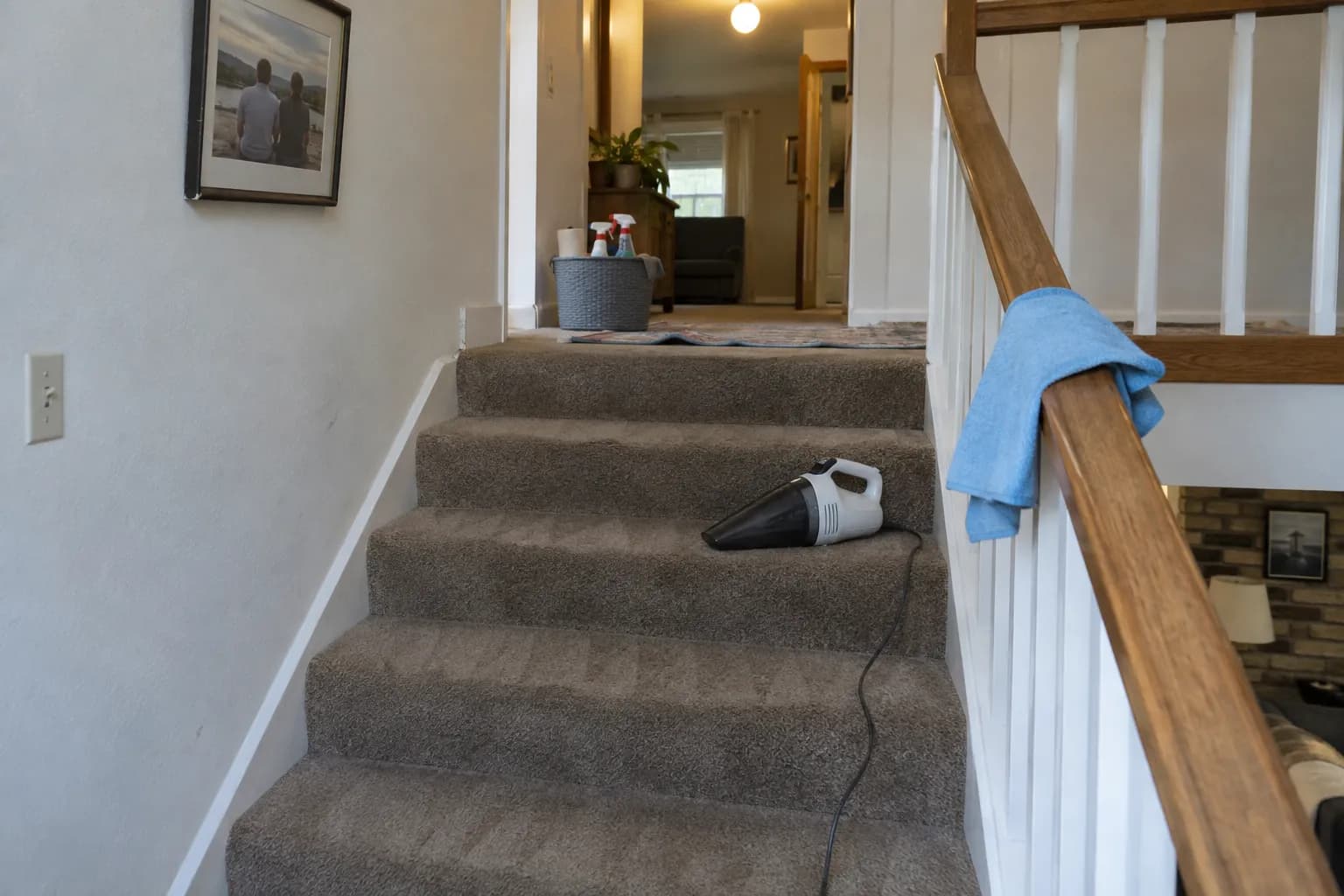 Carpeted staircase with a hand vacuum on one step and a blue cloth over the wooden handrail