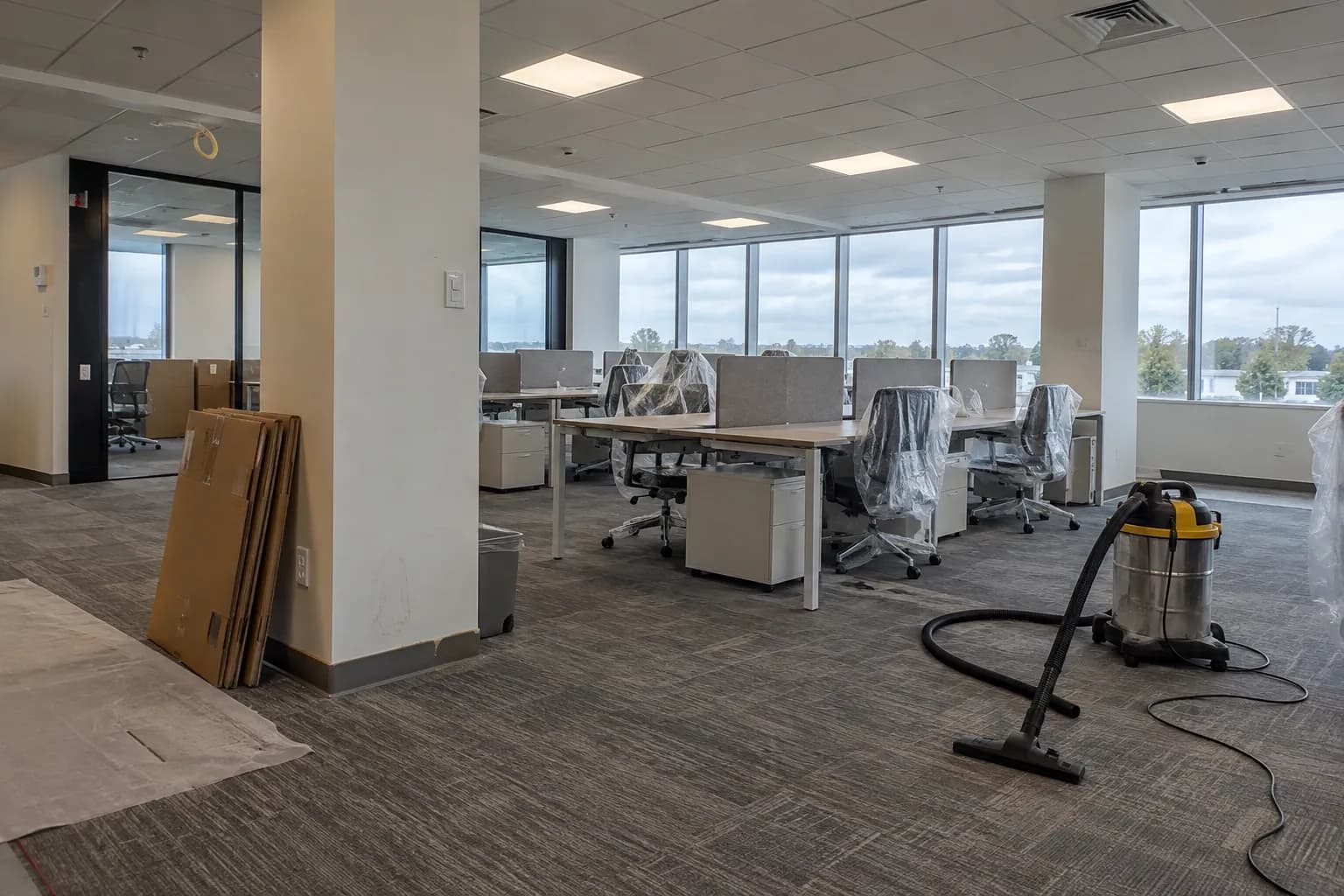 A newly fitted-out office with furniture still in plastic wrap and a shop vacuum ready for the cleanup